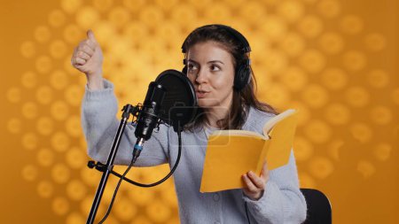 Voice actor looking to producer off camera to know when to start narrating book, producing audiobook. Narrator doing counting on fingers gesturing before starting digital recording of novel, camera B