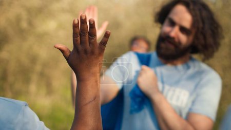 Photo for Team leader sharing a high five with her volunteers members after litter cleanup success, praising each other and feeling satisfied with nature preservation. Collecting rubbish and cleaning. Camera A. - Royalty Free Image