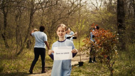 Photo for Portrait of sweet girl with save our planet poster against pollution and illegal dumping, volunteering to restore and preserve nature in the forest. Little child shows awareness sign. Camera B. - Royalty Free Image
