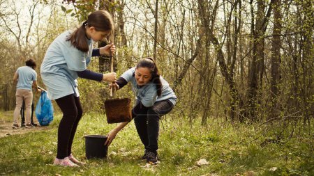 Mother and daughter team up to plant new trees in the woods, protecting the natural habitat and ecosystem. Family of activists fighting nature conservation, digging holes for seedlings. Camera B.