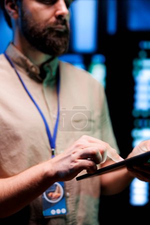 Photo for Manager in high tech facility using tablet to patch network issues affecting server cabinets performance and connectivity, leading to slow data transfer rates and weak client communication, close up - Royalty Free Image