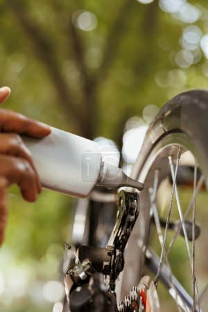 Tiro detallado de anillo de cadena de bicicleta que se lubrica con grasa especializada para un ciclismo de ocio al aire libre seguro. Imagen que muestra la vista de cerca del lubricante de cadena de mano afroamericano.