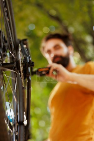 Image showing close-up view of bike rear derailleur and cogset being repaired and adjusted outside for leisure cycling. Detailed shot of young male cyclist checking tire as annual bike maintenance