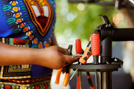 Photo for Close up of person choosing expert work tools for yearly outdoor bicycle maintenance. Detailed shot of female african american arm arranging an assortment of professional equipments. - Royalty Free Image