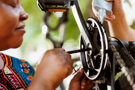 Photo for Close up of female african american using allen key to repair damaged bicycle crank-arm. Outdoor detailed shot of two people repairing and greasing bike chain and pedals for secure outdoor cycling. - Royalty Free Image