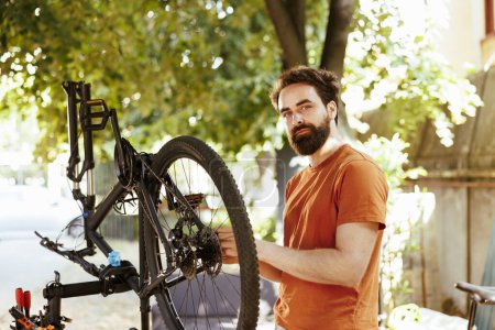 Retrato del ciclista masculino sano comprometido sosteniendo el neumático dañado de la bicicleta para la reparación y el mantenimiento en el patio del hogar. Activo deportivo caucásico hombre manejo rueda de bicicleta para el desmantelamiento.