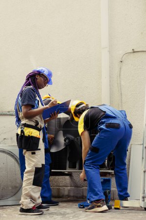 Photo for Diverse crew of trained engineers fixing air conditioner system electrical issues caused by faulty wiring or defective capacitor requiring professional intervention to diagnose and repair - Royalty Free Image