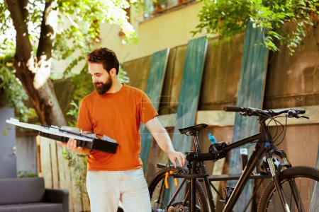 Photo for Image showing healthy athletic caucasian man holding his toolbox in home yard for bicycle maintenance. Sports-loving active male cyclist exploring professional equipments outside. - Royalty Free Image
