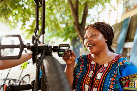 Photo for Vibrant sporty african american female fixes bicycle components with professional work tool from home yard. Active enthusiastic black woman outdoors using allen key to repair bike crank arm and pedal. - Royalty Free Image