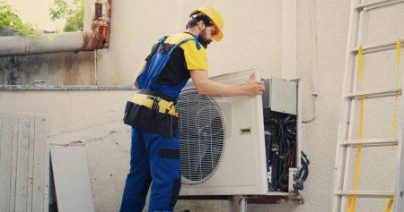 Precise serviceman starting work on malfunctioning outdoor air conditioner, dismantling condenser front coil panel. Proficient expert disassembling external hvac system to check for faulty wires