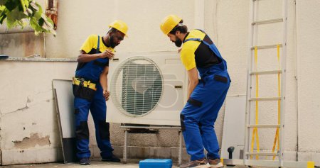 Photo for Certified technicians coworkers opening up rusty malfunctioning air conditioner to replace it with new performant outside condenser after draining refrigerant and replacing ductwork - Royalty Free Image
