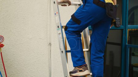 Reparador experto en uniforme profesional con equipo técnico escalando escalera plegable para hacer mantenimiento en el aire acondicionado de la azotea. Técnico eficiente encargado de chequear el sistema hvac