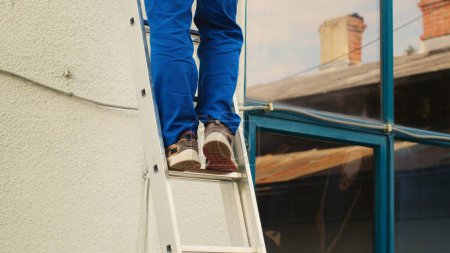 Photo for Certified technician holding cordless drill, stepping down from folding ladder after finishing checkup on rooftop condenser. Skilled expert at the end of maintenance assignment - Royalty Free Image