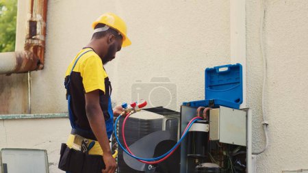 Qualified mechanic looking at freon levels in external air conditioner while using manifold meters to meticulously measure the pressure in condenser, ensuring efficient cooling performance
