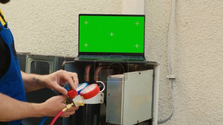 Photo for Skilled repairman contracted by client to detect condenser issues, checking real-time superheat and subcooling values measured by ac gauges vacuum pump displayed on green screen laptop - Royalty Free Image