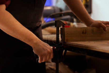 Holzarbeiter mit Schraubstock zum Halten von Holzklötzen, Beginn der Möbelmontage in der Werkstatt, Nahaufnahme. Handwerker in der Tischlerei mit Schraubstock Werkzeug, um Stück Holz vor der Schnitzerei klemmen