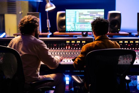 Chanteur et producteur travaillant ensemble dans un studio de musique professionnel, collaborant sur une chanson à succès dans la salle de contrôle. Ingénieur audio édition des enregistrements avec techniques de mixage et de mastering.