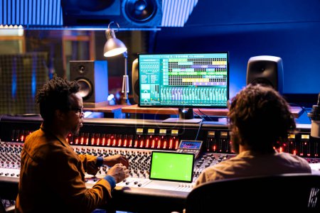 Musicien et producteur sonore regardent la maquette isolée sur tablette, en utilisant des techniques de mixage et de mastering pour créer des chansons. Équipe de musiciens éditant de la musique avec application logicielle audio numérique.