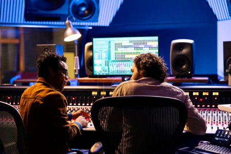 Photo for Team of sound technician and singer working on new music, mixing tunes on digital software in control room. Musician and producer collaborating on a new album, mixing and mastering tracks. - Royalty Free Image