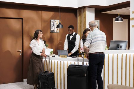 Männliche und weibliche ältere Gäste in der modernen Hotellobby, mit aufmerksamem Personal, das effizient beim Check-in und bei der Reservierung hilft. Ältere Touristen warten mit Koffern an der Rezeption.