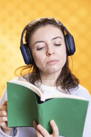 Mujer que se concentra en la lectura del libro, relajante y escuchar el ruido de audio blanco, aislado sobre el fondo del estudio. Geek con canciones novedosas en la mano a través de auriculares, concepto de entretenimiento