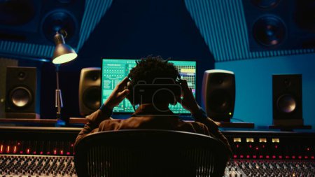 Photo for Sound designer editing tracks by adjusting volume levels with panel board knobs and sliders, studio control room. Audio technician mixing and mastering hit song with digital software. Camera B. - Royalty Free Image