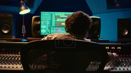 Audio expert does mixing and mastering on tracks using digital editing software in studio, producing new music. Skilled sound designer adjusting volume levels by using switchers and faders. Camera B.