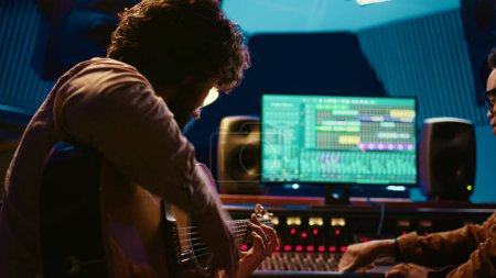 Photo for Young artist songwriter composing a new song on guitar in recording session at studio, creating tunes and editing them after in post production. Musician composer producing tracks. Camera B. - Royalty Free Image