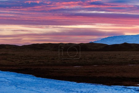 Spektakulärer Sonnenuntergang in der Nähe frostiger Hügel in Island, Konzept für Nachtaufnahmen. Majestätische isländische Landschaften mit Sonnenuntergang über Feldern, die einen atemberaubenden Blick auf den Himmel aus rosa Zuckerwatte bieten.
