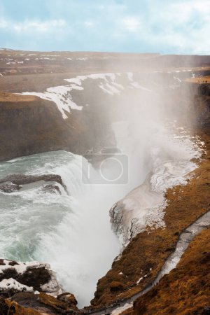 Téléchargez les photos : La chute d'eau pittoresque de Gullfoss dans la nature arctique offre un paysage glaciaire avec des pâturages enneigés et de l'eau gelée coulant des collines. Beauté du Nord à flanc de colline en Islande. - en image libre de droit