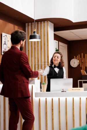 Front desk staff hands out access card for businessman, ensuring comfortable and hassle free stay at luxury hotel. Receptionist with impeccable customer service providing room key after long trip.
