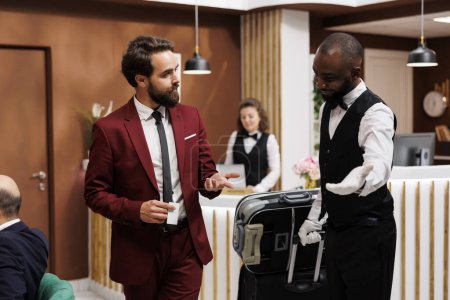 Bellboy taking guest to his hotel room, providing excellent luxury service for businessman with luggage. Bellhop carrying suitcase for traveller, formal client on business trip.