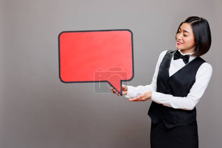 Photo for Smiling asian waitress showing red empty message banner mockup for restaurant advertising. Cafe woman employee in uniform holding blank chat bubble with copy space for promotion - Royalty Free Image