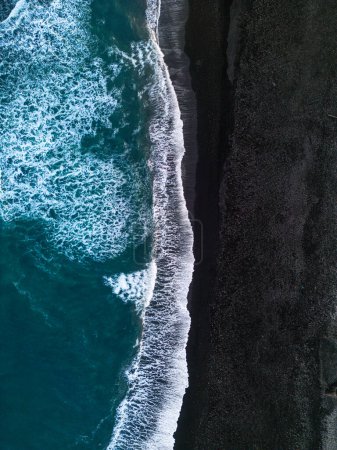 Foto de Vista aérea de la playa islandesa de arena negra con increíbles playas atlánticas con olas fuertes. Escena fría en el norte con montañas cubiertas de nieve y costas arenosas con arena negra. - Imagen libre de derechos