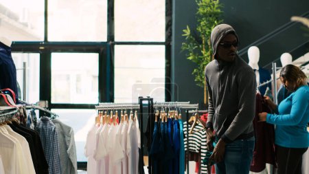 Foto de Ladrón afroamericano robando ropa, huyendo de una boutique moderna. El guardaespaldas asiático atrapa a ladrón en la puerta de la tienda, lo amenaza con la policía en el centro comercial. Concepto de robo - Imagen libre de derechos