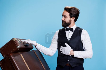 Male bellhop points left and right to create new advertisement, indicating direction sideways while he wears formal attire. Young classy doorman presents ad over blue background.