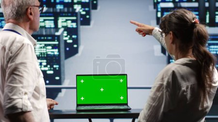 Coworkers in server farm housing high end processors capable of quickly and efficiently performing complex computations and data analysis, using green screen laptop to fix malfunctions