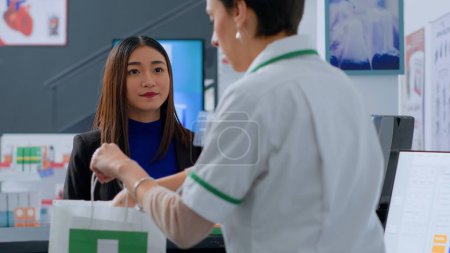 Photo for Senior pharmacy assistant helping asian client pick ideal medicinal products for ameliorating pain before reaching drugstore counter. Customer purchasing wellness supplements and vitamins - Royalty Free Image