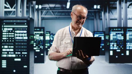 Capable serviceman expertly managing data while navigating in industrial server room. Proficient repairman in high tech facility ensuring optimal cybersecurity protection, optimizing systems