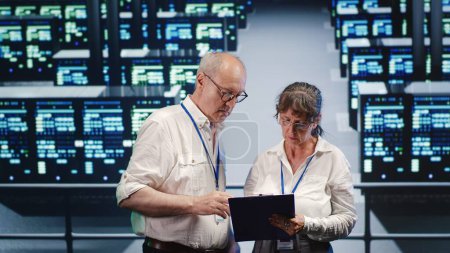 Cloud computing business executives looking around data center, using clipboard to crosscheck disaster recovery plan and assess high tech workplace servers in need of replacement, preventing concerns