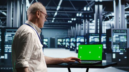 Developer in server room expertly managing data while navigating through industrial mainframes. Expert ensuring flawless cybersecurity guard, optimizing systems using green screen laptop