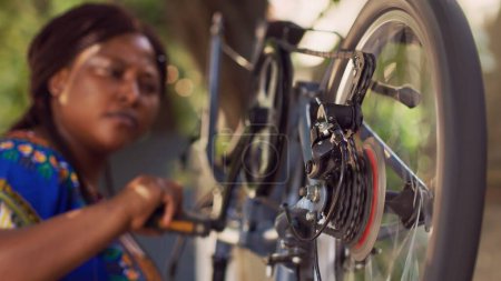 Photo for Detailed view of bicycle chain ring crank and barrel adjuster carefully examined and adjusted outside by african american lady. Close-up shot of black woman thoroughly inspecting bicycle cassette. - Royalty Free Image