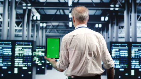 Tech savvy specialist expertly managing data while navigating through industrial supercomputers. Expert ensuring flawless cybersecurity shielding, optimizing systems using green screen tablet