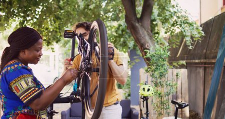 Auf dem Hof wechseln aktive sportbegeisterte Freunde und Freundinnen Fahrradreifen mit Arbeitsgeräten für die jährliche Wartung. Gesundes multiethnisches Paar inspiziert und repariert Fahrradzubehör für Outdoor-Radtouren.