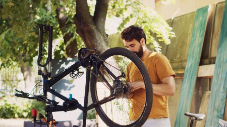 Photo for Active man outside demonstrating commitment to repairing and securing bicycle components for summer cycling leisure. Caucasian male selecting professional equipment for bike maintenance. - Royalty Free Image
