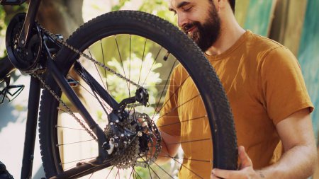 Photo for Energetic fit caucasian man outside repairing and maintaining bicycle components using specific tools. Male cyclist carefully examining and fixing damaged bike with great enthusiasm. - Royalty Free Image