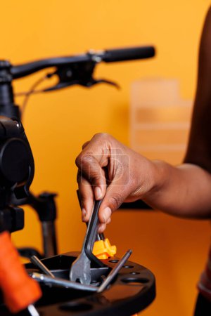 Schwarze Frauenhand in Nahaufnahme bei der Auswahl und Analyse von Geräten aus der Fahrradwerkstatt. Fotofokus auf spezielle Fahrradwartungswerkzeuge, die von einer afrikanisch-amerikanischen Frau gehalten und arrangiert werden.