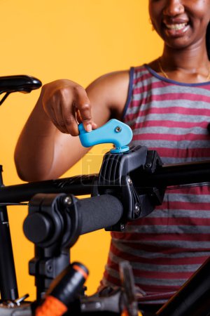 Black woman grips bicycle frame and securing it on repair stand against isolated background, showcasing dedication to cycling maintenance. Close-up of female holding the bike workstand clamp.