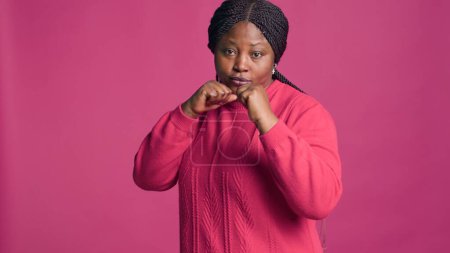 Confident black woman with her hands clasped together showing ready for fighting. African american lady with self-confidence posing with clenched fists against pink color background.