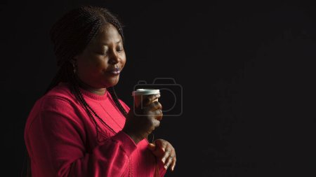 Photo for African american woman immersed in pleasure of sipping coffee lost in contemplation gazing upwards. Female fashion blogger savors her warm beverage with sense of satisfaction. Side-view portrait. - Royalty Free Image